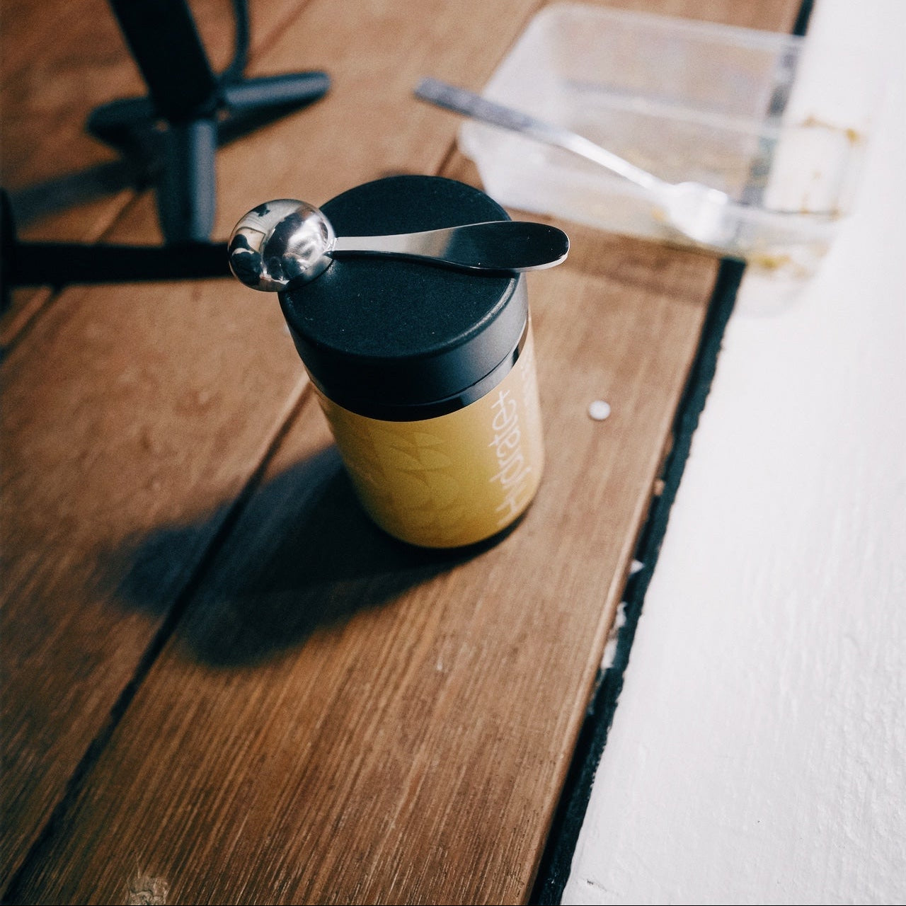 Small container with black lid and spoon on a wooden surface