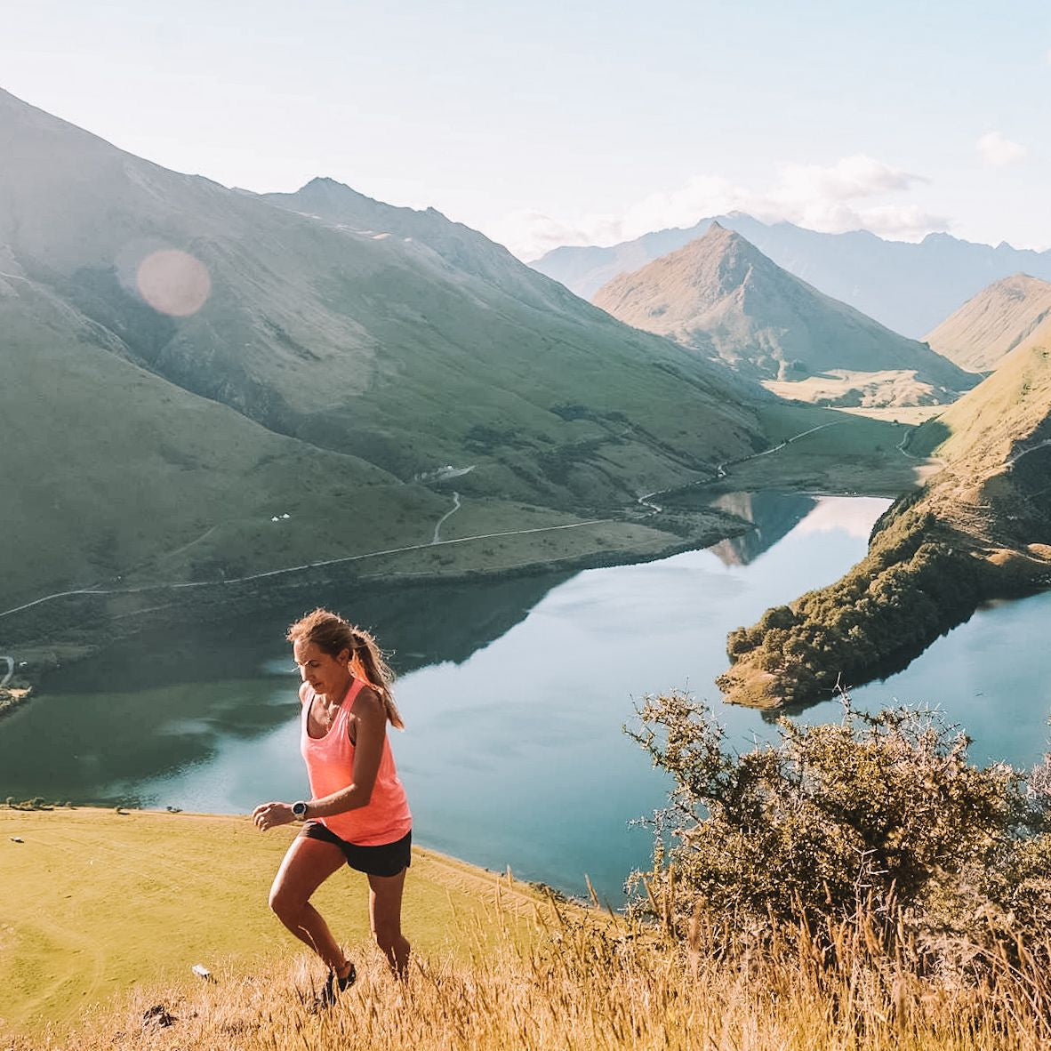 Woman running on a hill with a scenic view of mountains and a lake.